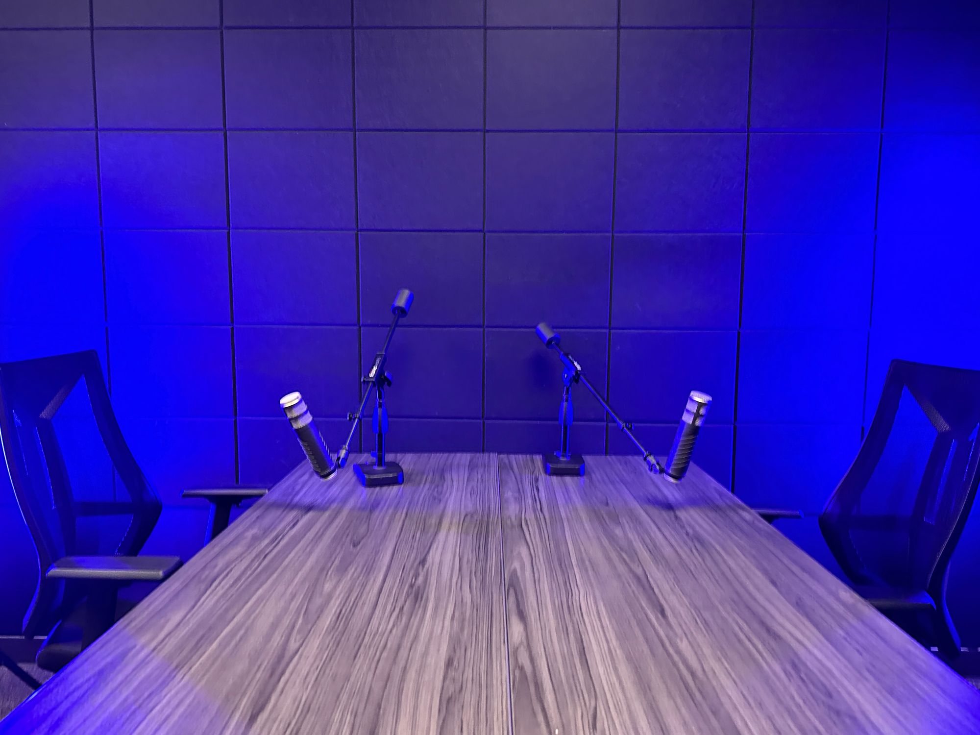 The Content Factory A modern recording studio setup in Austin, Texas features two black chairs, a wooden table, two microphones, and blue lighting. In Austin, Texas