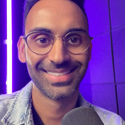 The Content Factory A person wearing glasses and a denim jacket smiles at the camera, holding a microphone in what looks like The Content Factory's podcast studio, with a purple neon light in the background. In Austin, Texas